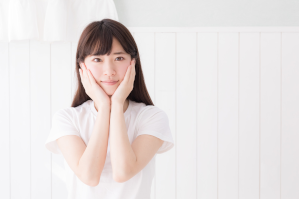 顎に両手をあてている白い服を着た女性