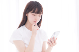 スマホを持ちながらあごに手を当てて考え事をしている女性