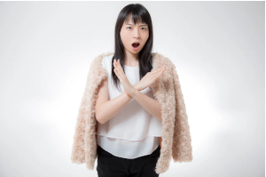 女性が胸当たりで大きなバツを腕で作っている