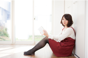 壁に寄りかかり本を持った女性がこっちを見ている