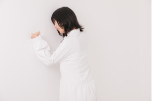 白い服を着ている女性が、悔しがりながら壁を叩いている