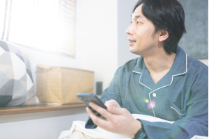 ベッドの上でスマホを持ちながらパジャマを着た男性