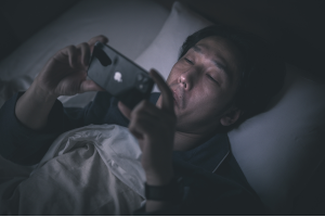 暗い部屋でベッドに入りながらスマホを見ている男性