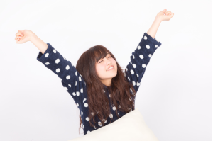 ドット柄のパジャマを着た女性がベッドの上で背伸びをしている