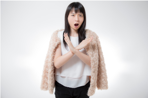 女性が胸当たりで大きなバツを腕で作っている