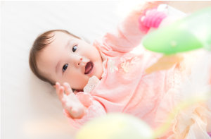 仰向けになって手を挙げている女の子の赤ちゃん