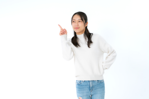 白い服を着た女性が右手人差し指を立てて斜め上を見ている