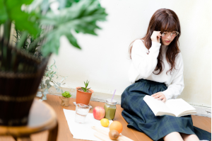眼鏡をかけた女性が床に座って本を読んでいる