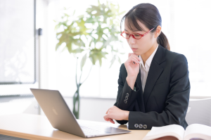 パソコンを見ながら悩んでいる赤い眼鏡をかけたスーツの女性