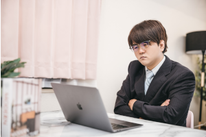 スーツを着た男性がパソコンを見ながら悩んでいる