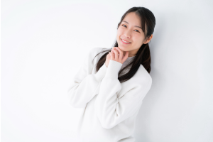 白い服を着た女性が両手をあごに当てて微笑んでいる