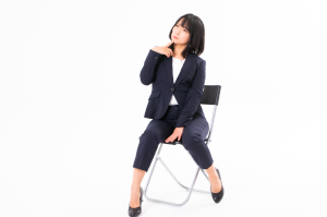 椅子に座ったスーツの女性があごに手をあてて考え事をしている