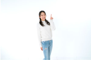 白い服を着た女性が人差し指を立ててこっちを見て笑っている