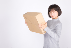 タートルネックを着た女性が包装された箱を持ってこっちを見ている