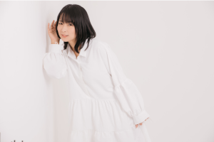 壁に耳をあてて何かを聞いている白いワンピースを着た女性