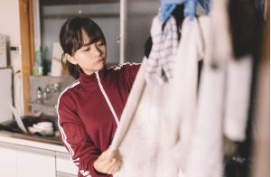 赤いジャージを着た女性が、洗濯物を触って考えている
