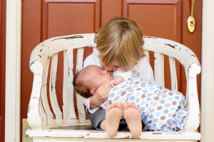 ベンチに座った子供が抱っこした赤ちゃんにキスをしている