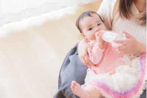 ママの膝の上でミルクを飲んでいる赤ちゃん