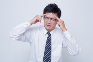 両手でおでこをおさえているスーツの男性