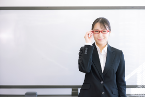 ホワイドボードをバックに赤い眼鏡をかけたスーツの女性