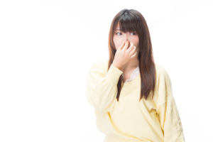 黄色い服を着た髪の長い女性が鼻をおさえている
