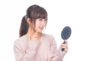丸い手鏡を持った女性が顎を指しながら困っている