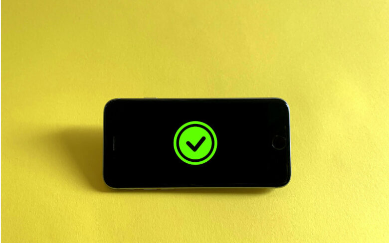 黄色い背景の上に置かれたスマートフォンに、緑色のチェックマークが大きく表示されている。