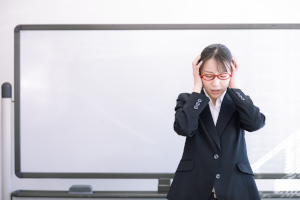 赤い眼鏡をかけたスーツの女性が頭を抱えている
