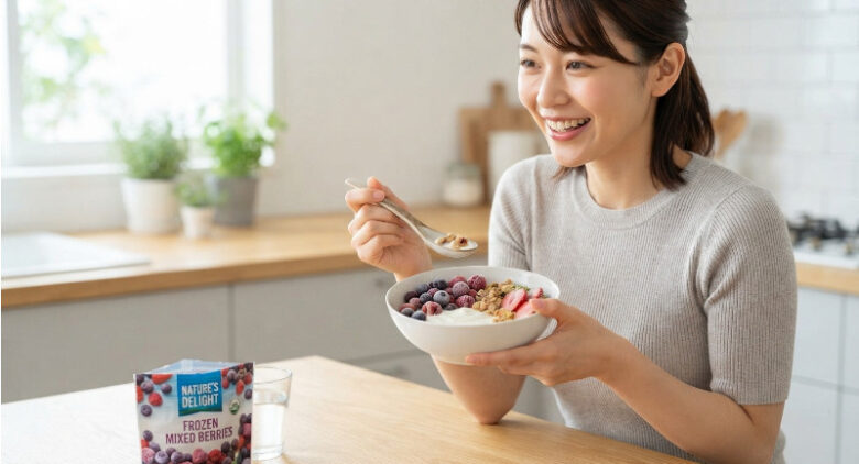笑顔の女性が、冷凍のミックスベリーやグラノーラがトッピングされたヨーグルトを美味しそうに食べている様子。