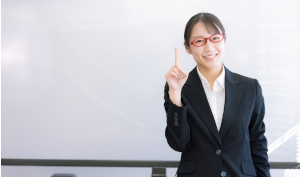 赤い眼鏡をかけたスーツの女性が人差し指を立てている