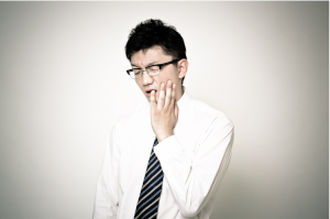 眼鏡をかけた男性が、左頬を押さえて痛がっている