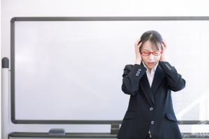 赤い眼鏡をかけたスーツの女性が頭を抱えている