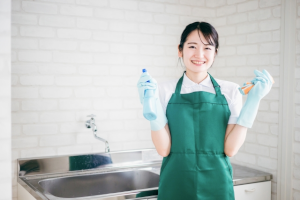 両手に掃除道具を持った緑色のエプロンの女性