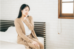 ベッドに座った女性が左頬を押さえて痛がって