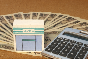 電卓とコンビニと書かれた積木の下に並べられた数枚の1万円札