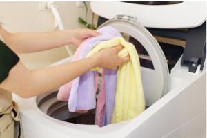 洗濯物に3色のタオルを入れる女性
