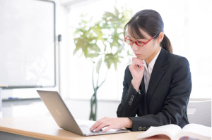 赤い眼鏡をかけたスーツの女性が悩んでいる