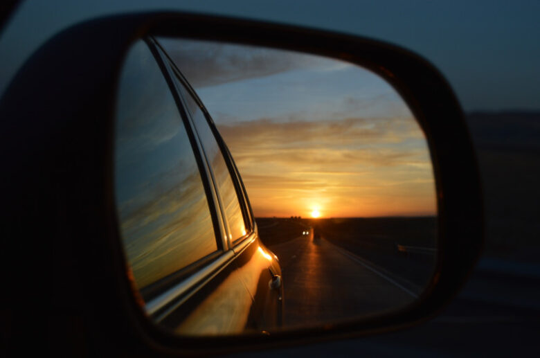 黒い車のサイドミラーに美しい夕焼け空が映り込んでいる様子