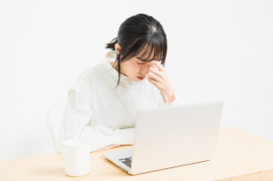 パソコンの前に座っている女性が眉間に手をあてている
