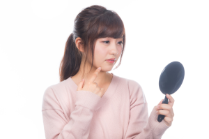 手鏡で顎に指をあてて悩んでいる女性
