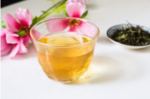 お茶が入ったコップとピンクの花とお茶の葉