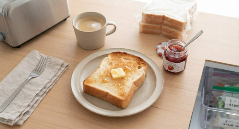 適切に冷凍・解凍され、こんがりと焼けた厚切りトーストが皿にのり、バターとジャム、コーヒーが添えられた朝食シーン。