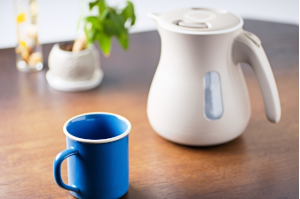 机の上に電気ケトルと青いコップ